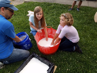 Instructor and kids mixing oobleck outdoors on the grass