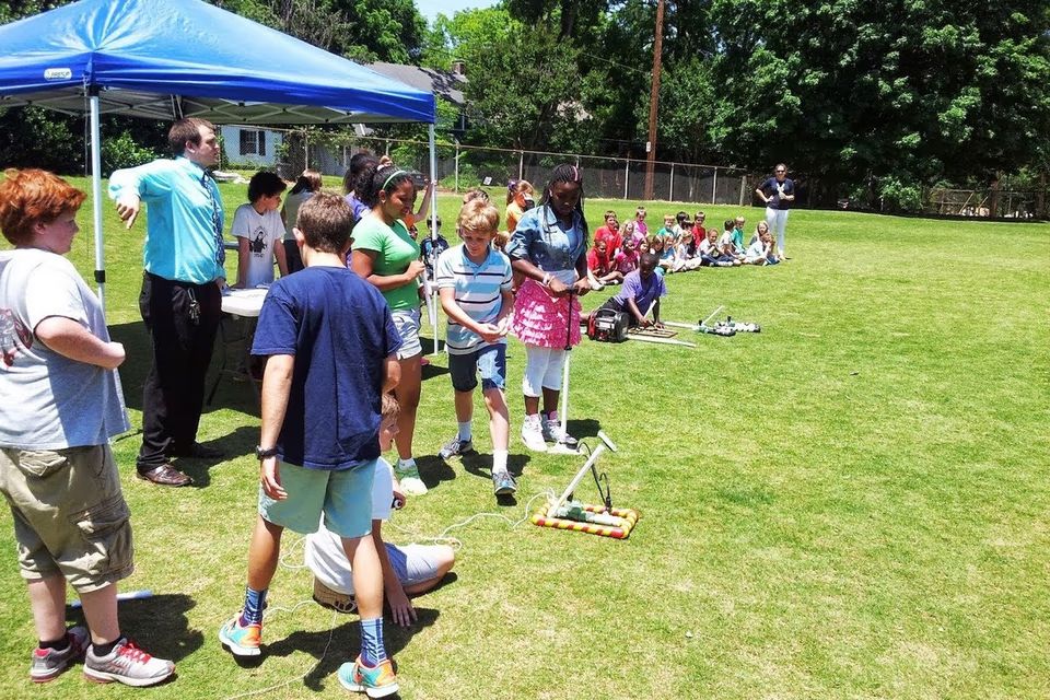 Students gathered on a sunny school field taking turns launching compressed air rockets with an instructor supervising