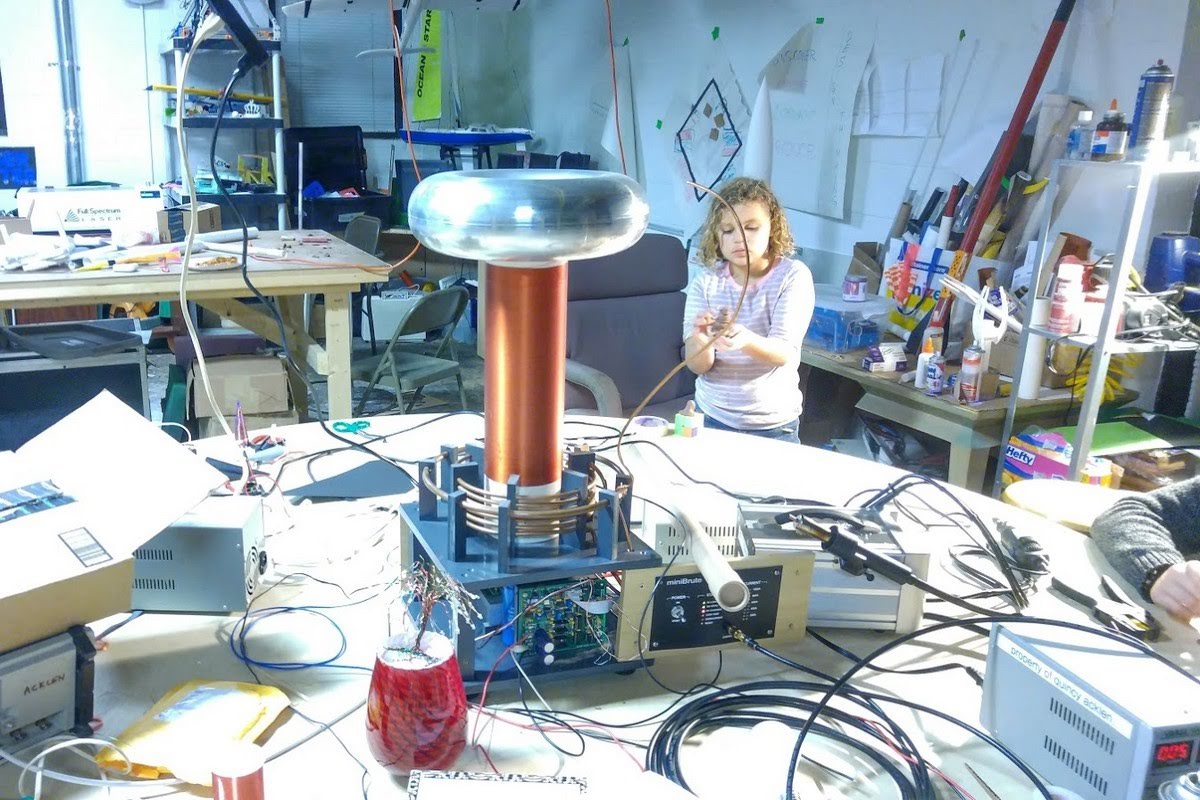 Large Tesla coil with copper windings and aluminum toroid in a maker workshop, demonstrating high voltage electromagnetic phenomena