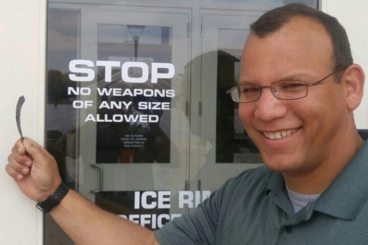 Quincy grinning while holding a tiny forged sword next to a 'No Weapons of Any Size Allowed' sign
