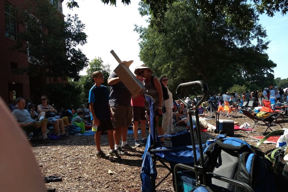 Crowd gathered outdoors for a total solar eclipse viewing event, with people using special viewing equipment and telescopes to safely observe the eclipse